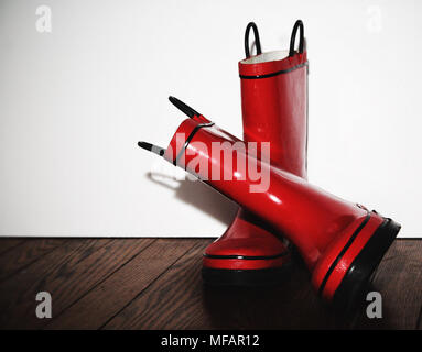 A pair of red child`s rainboots against the wall on a hardwood floor in the bedroom. Stock Photo